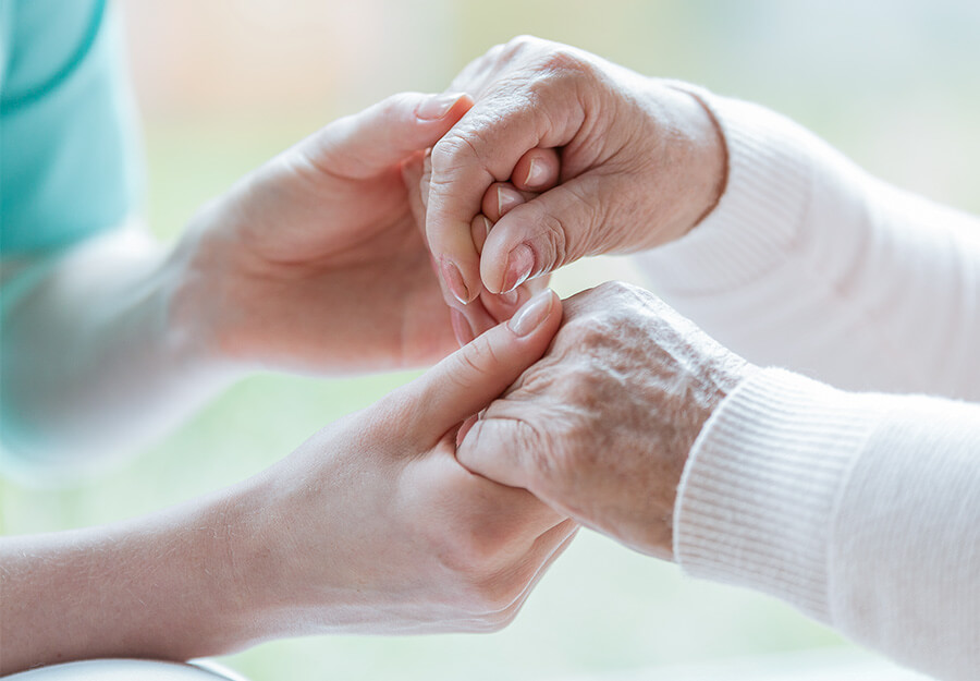 Caregiver holding hands with an elderly person, symbolizing support and trust.