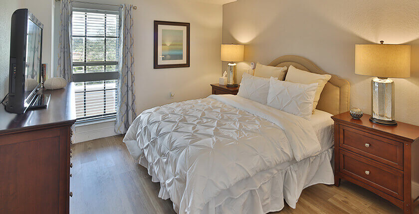 Cozy bedroom with a bed, lamps on nightstands, dresser, and a window with blinds.