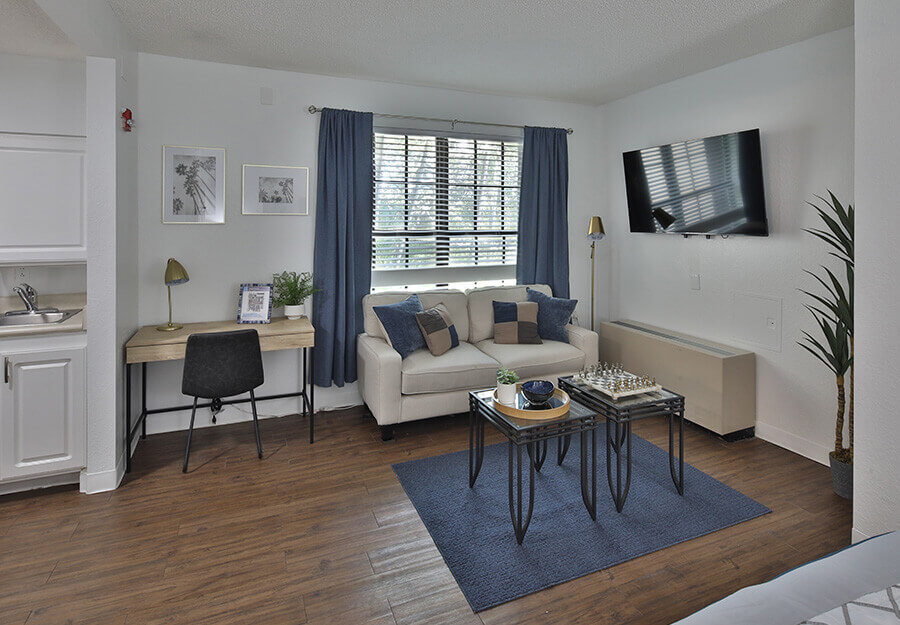 Comfortable living area in a unit with a couch, desk, wall-mounted TV, and natural light.