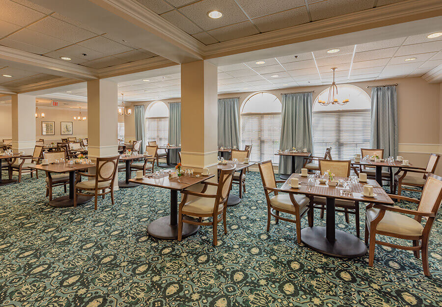 Elegant dining room with neatly set tables and comfortable chairs in a senior living community.