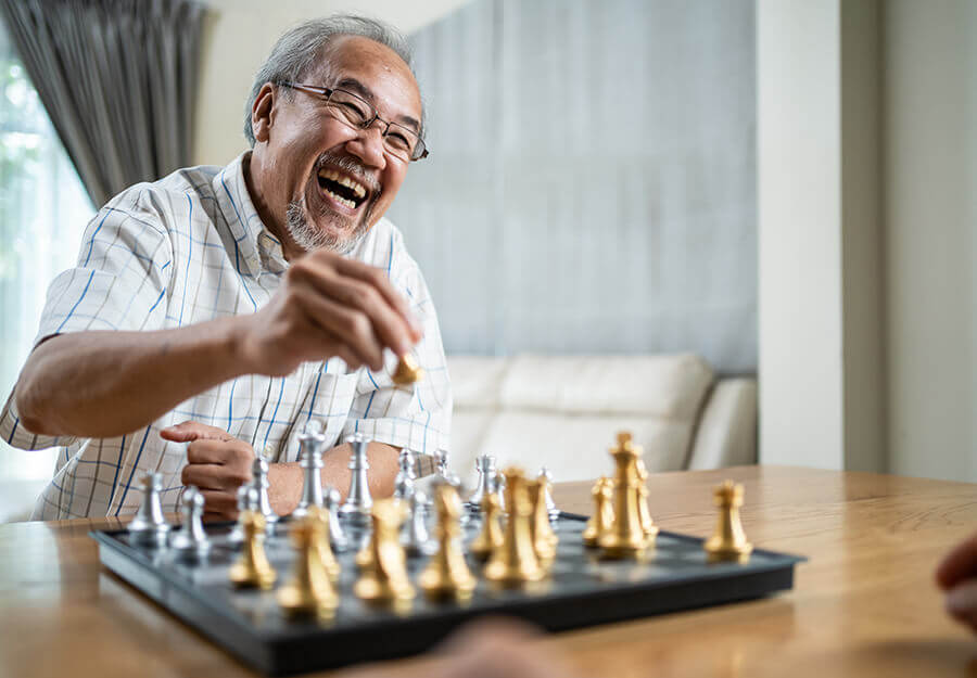 Smiling elderly man enjoying a game of chess in a bright, modern living space.