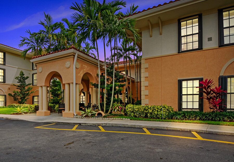 Elegant entrance of a senior living community building with palm trees and nicely landscaped grounds.