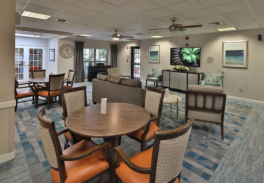 Comfortable lounge area with round table, chairs, and sofas in a senior living community.