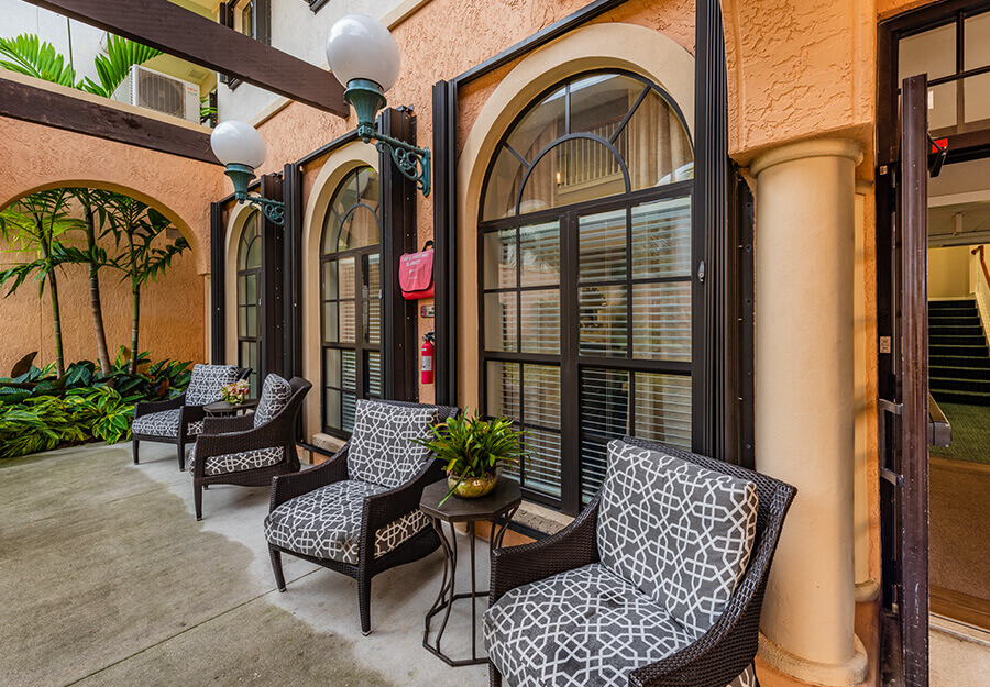 Outdoor seating area with patterned chairs and arched windows at a senior living community.