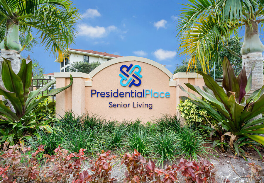 Sign for Presidential Place Senior Living surrounded by lush greenery and palm trees.