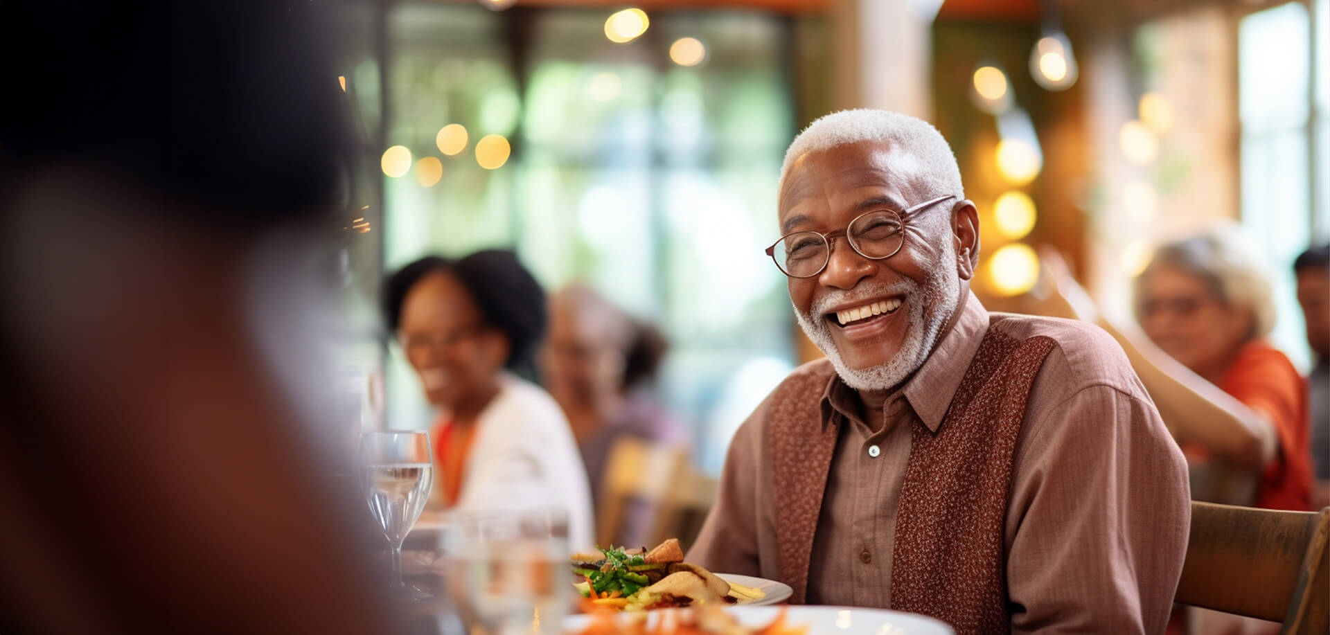 Smiling resident enjoying a meal in a lively dining area at a senior living community.