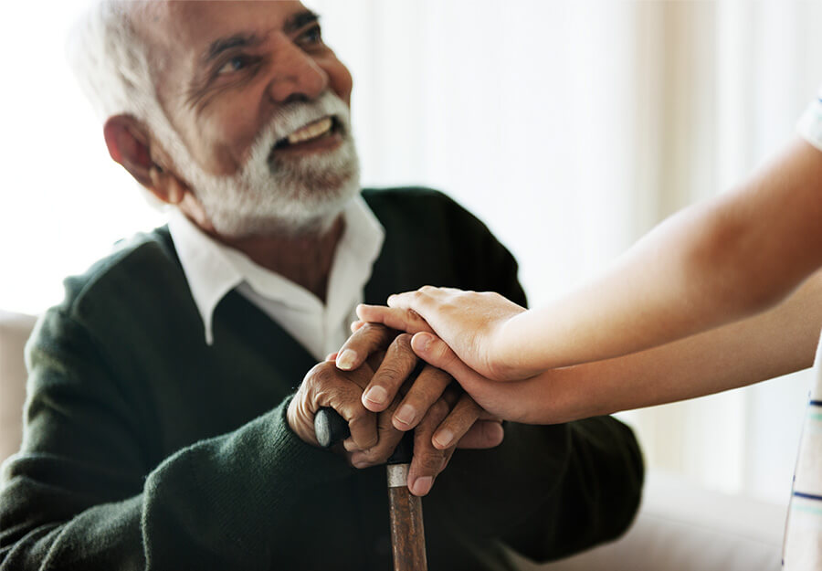 Senior man smiling and holding hands with a young person in a caring gesture.