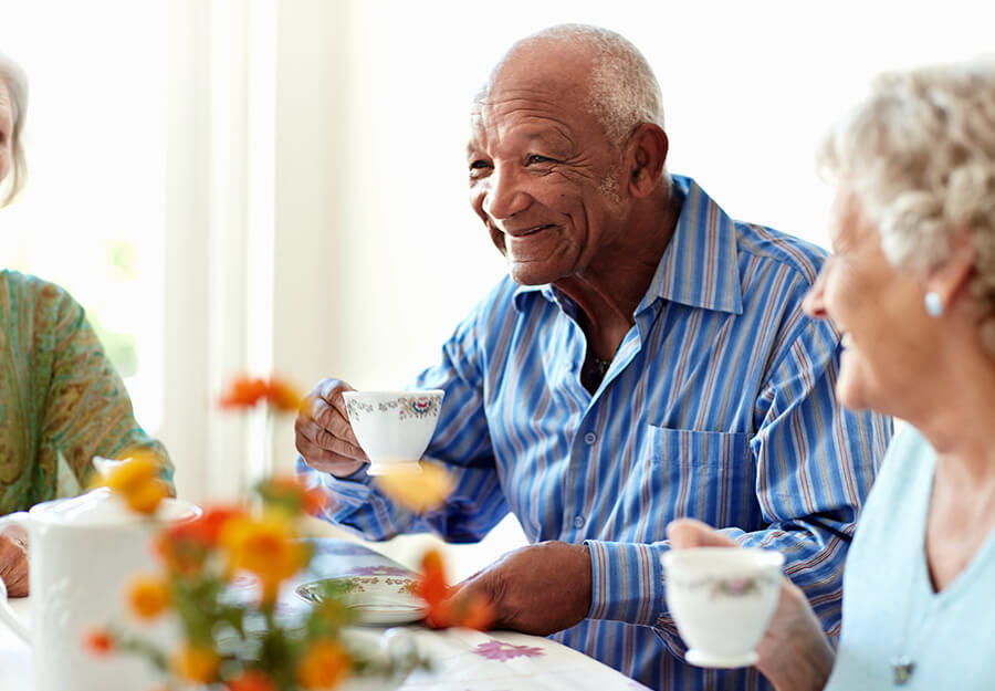 Senior man enjoying tea with friends in bright dining area, smiling and holding a teacup.