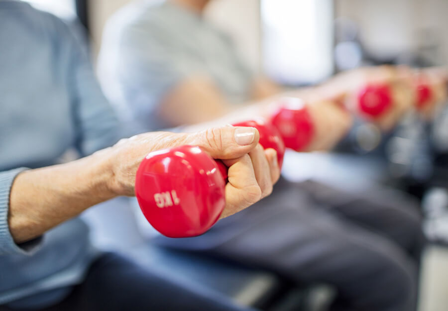 Close-up on senior individuals exercising with red hand weights in a community fitness area.