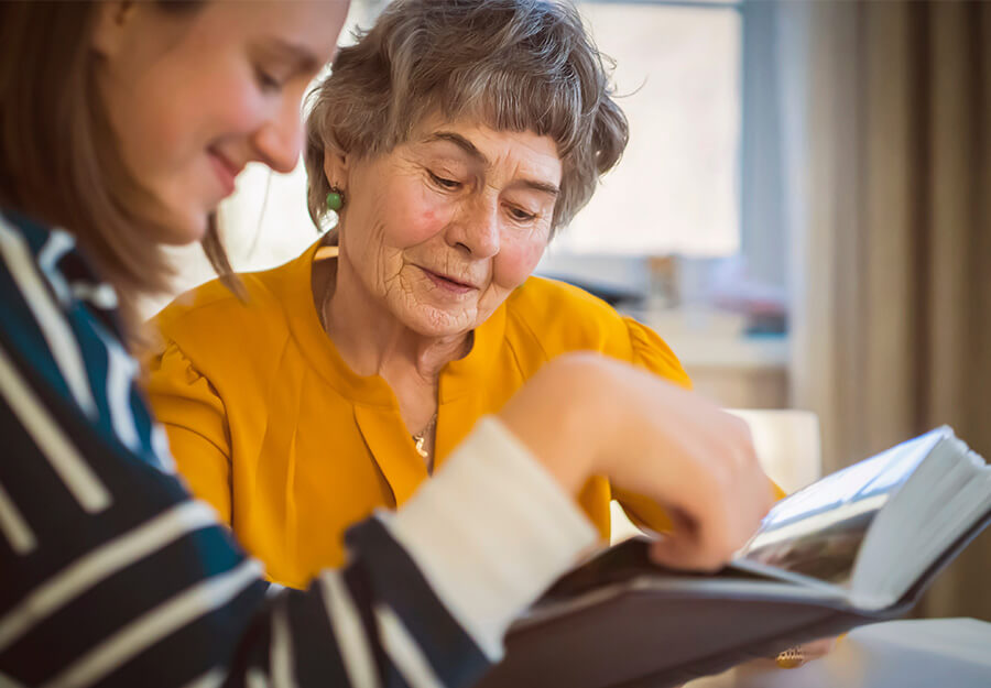 Elderly woman and young woman looking at a photo album together in a sunny room.