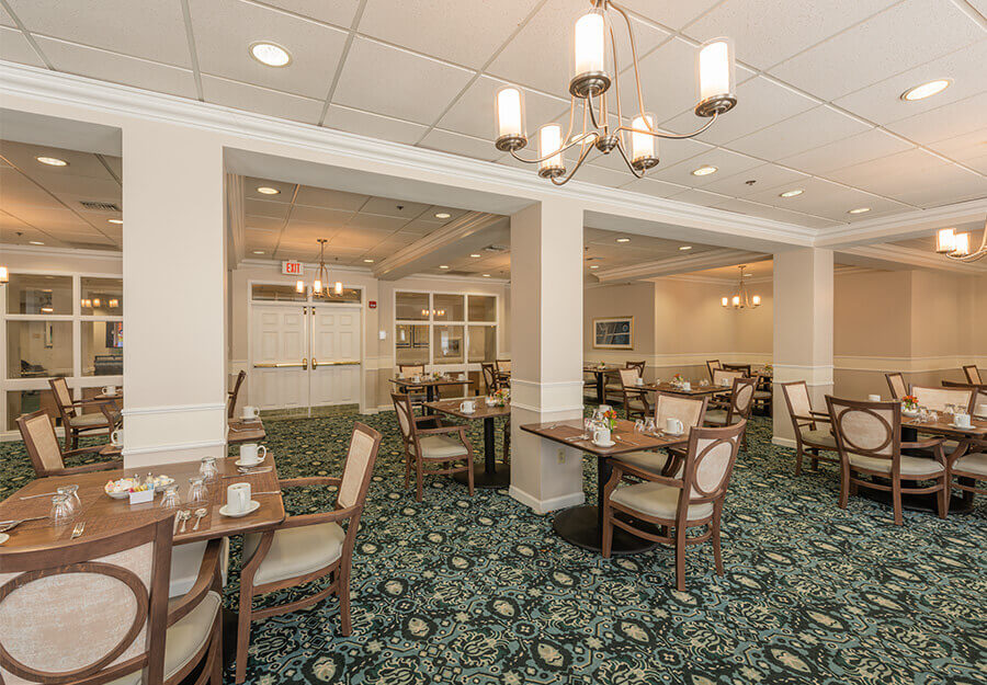 Spacious dining area with multiple tables and chairs in a senior living community.